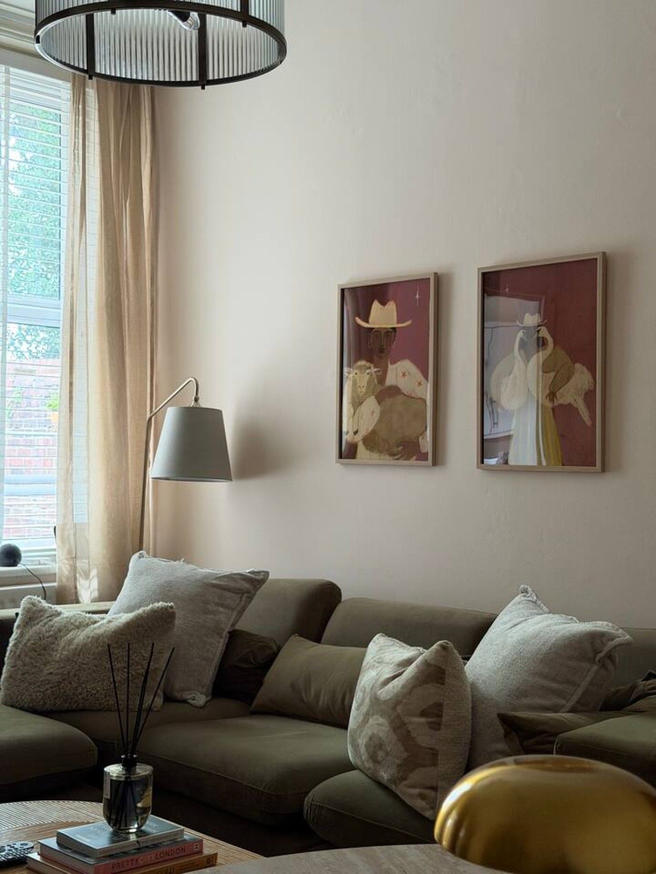 Ein Wohnzimmer mit einer Couch, einer Lampe und zwei gerahmten Kunstwerken an der Wand.
