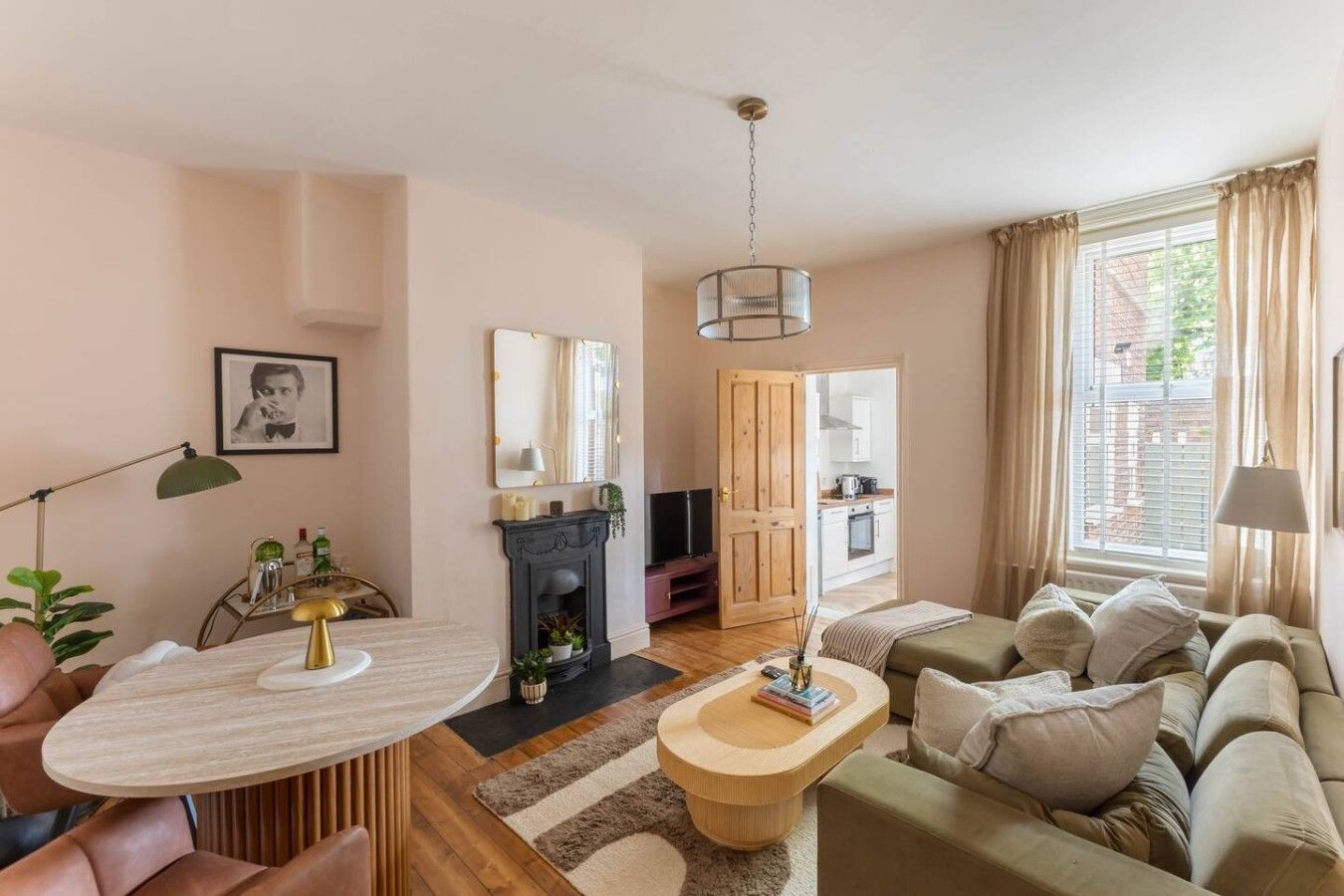 A cozy living room with a fireplace, a sofa, a dining table, and a kitchen visible through an open door.