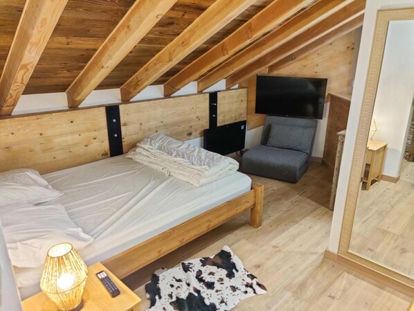 A bedroom with a wooden ceiling, a bed, a chair, a TV, and a small table with a lamp. - 40m from ski slopes, 3rd floor, fitness, swimming pool, sauna, balcony, tv, ski locker, 51m² (Les Orres)