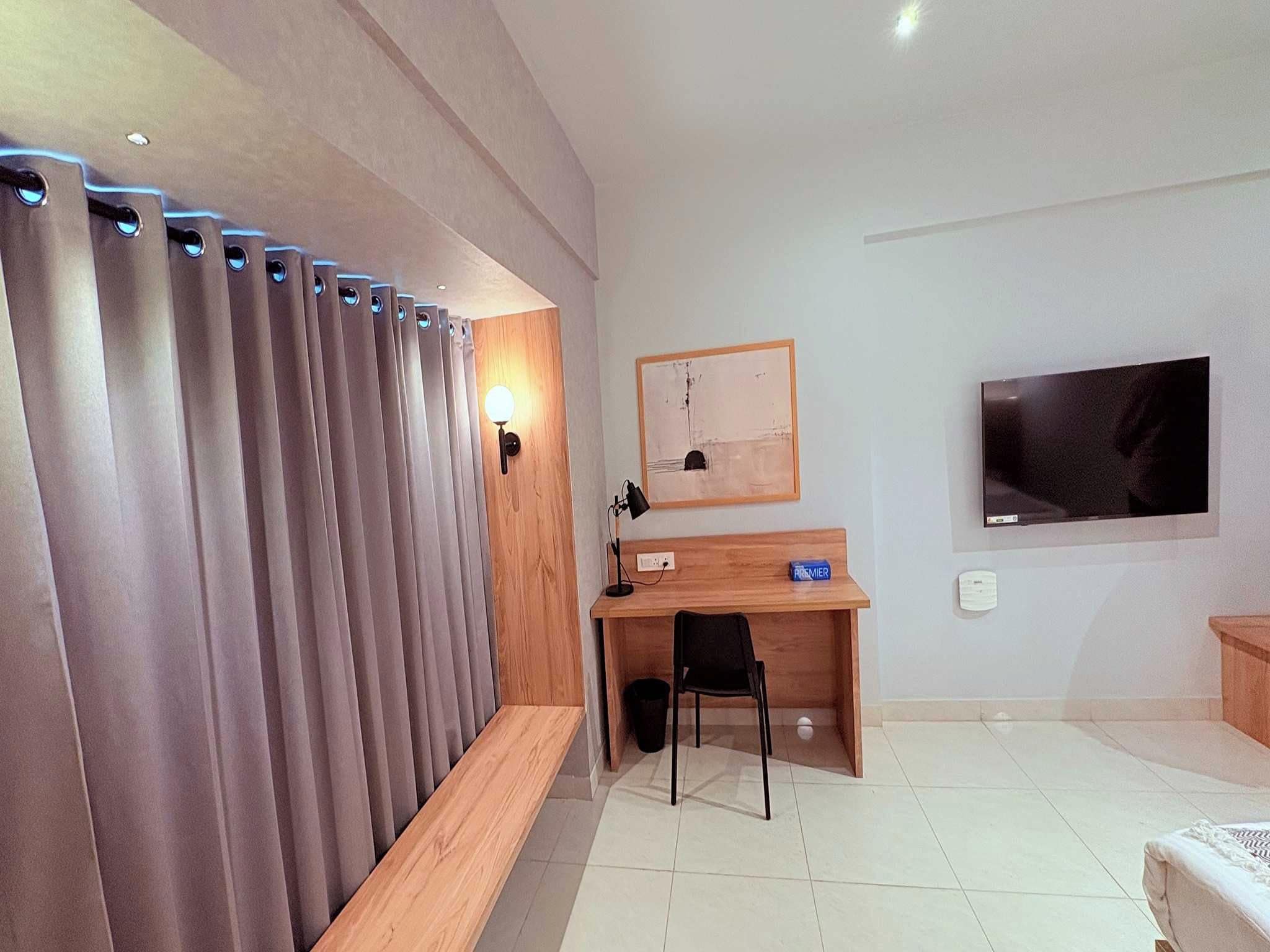 A modern hotel room with a bed, a desk, a chair, a TV, and a curtain.