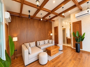 Una sala de estar moderna con un sofá modular, vigas de techo de madera y una planta grande en maceta.