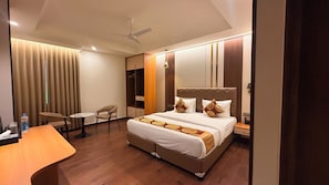 Una habitación de hotel con cama, escritorio, silla, armario y ventilador de techo.