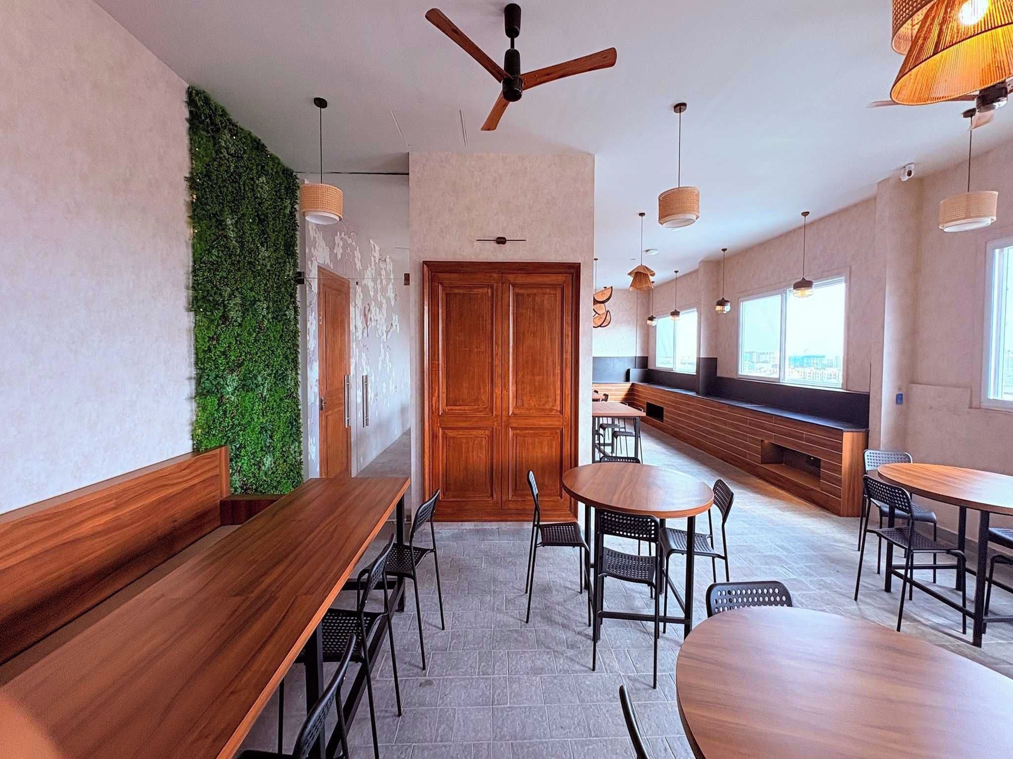 Un comedor moderno con mesas y sillas de madera, una pared verde y un ventilador de techo.