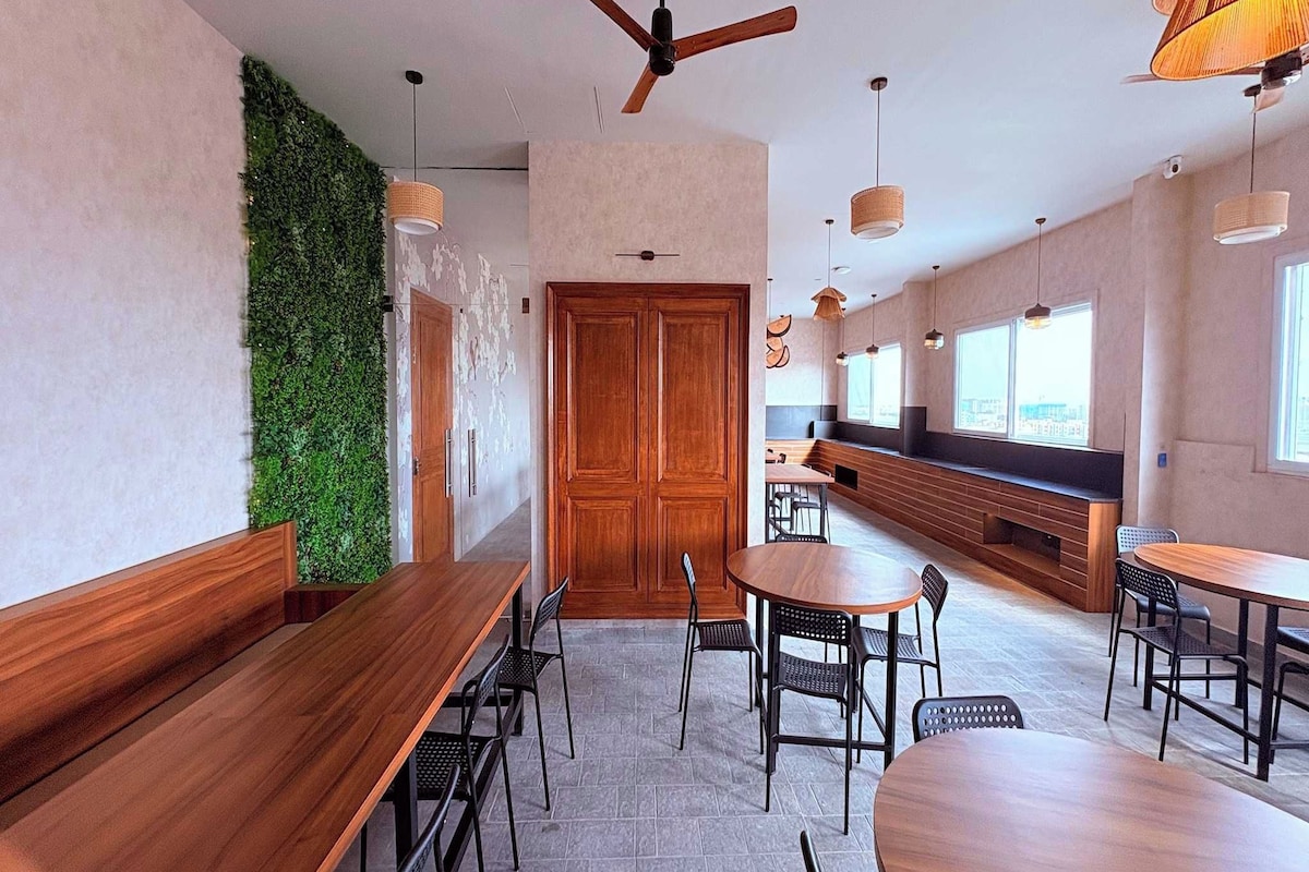Un comedor moderno con mesas y sillas de madera, una pared verde y un ventilador de techo.