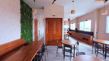 Un comedor moderno con mesas y sillas de madera, una pared verde y un ventilador de techo.