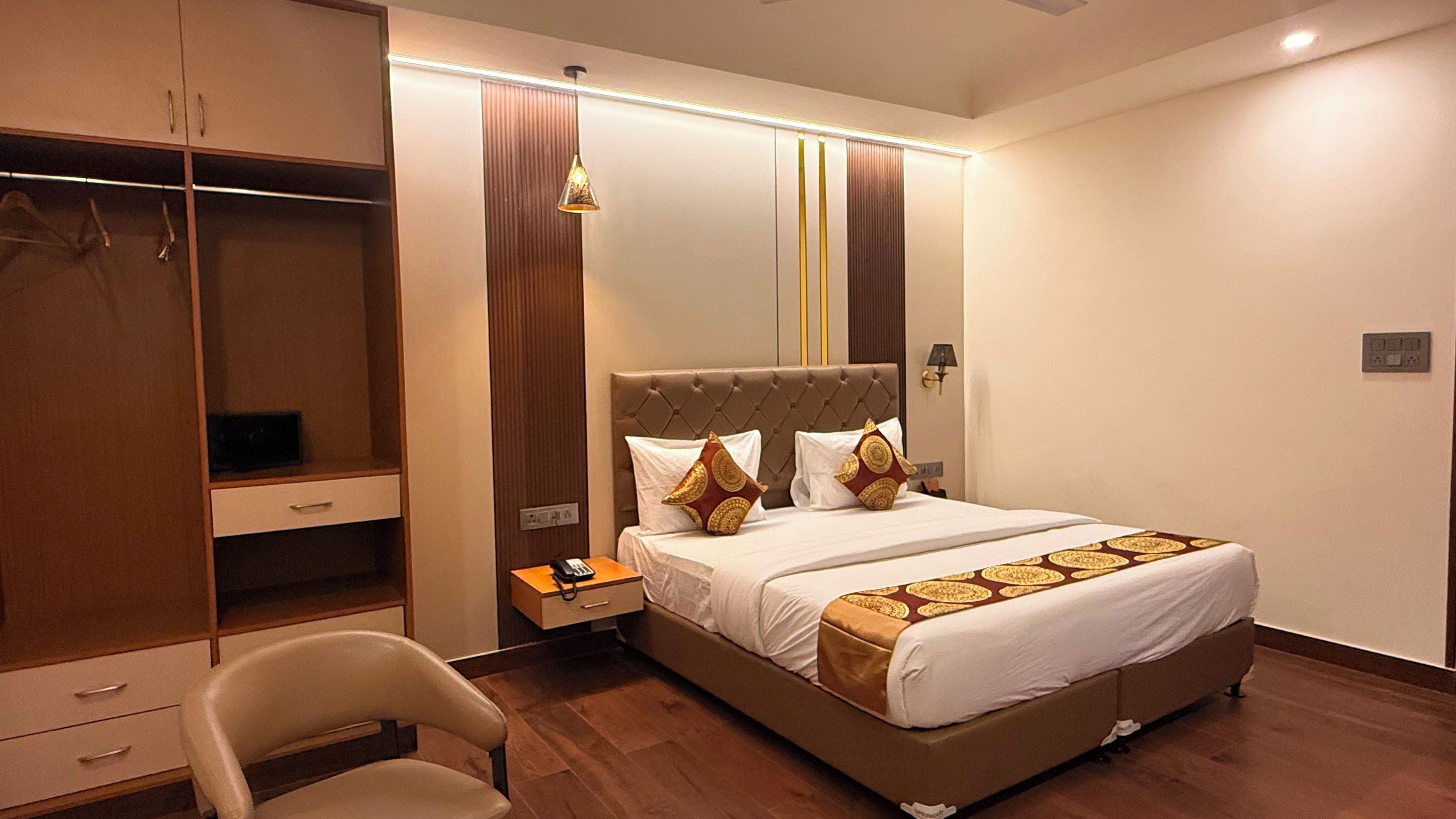 A hotel room with a bed, a desk, a chair, a wardrobe, and a bedside table.