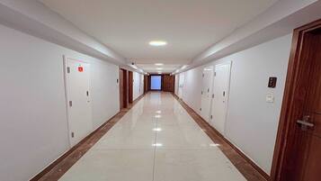 Un long couloir étroit, avec des portes de chaque côté, qui mène à une pièce lumineuse au bout.