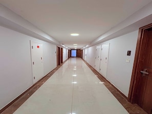 Un pasillo largo y estrecho con puertas a ambos lados, que conduce a una habitación luminosa al final.