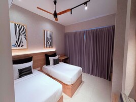 A hotel room with two beds, a ceiling fan, artwork on the walls, and a window with curtains.