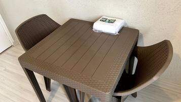 Uma mesa pequena e quadrada com tampo trançado e duas cadeiras de vime. Um travesseiro branco está sobre a mesa.
