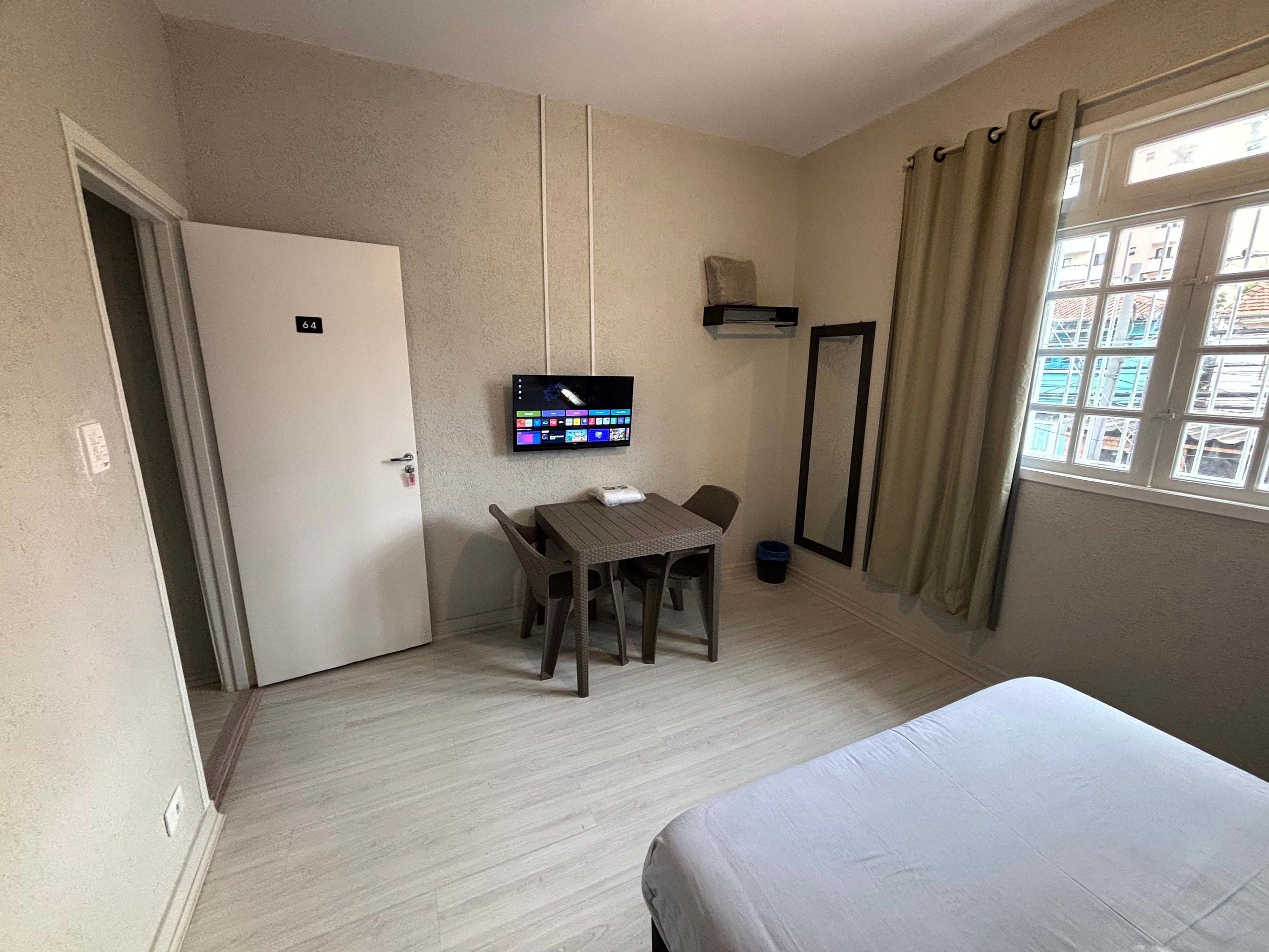 Una habitación de hotel con cama, escritorio con silla, televisión y ventana con cortinas.