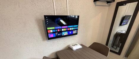 A wall-mounted TV displaying various apps and a table with chairs in a room with a textured wall and a mirror.