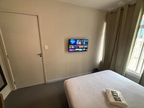 Habitación de hotel con cama, televisor montado en la pared, puerta y ventana con cortinas.