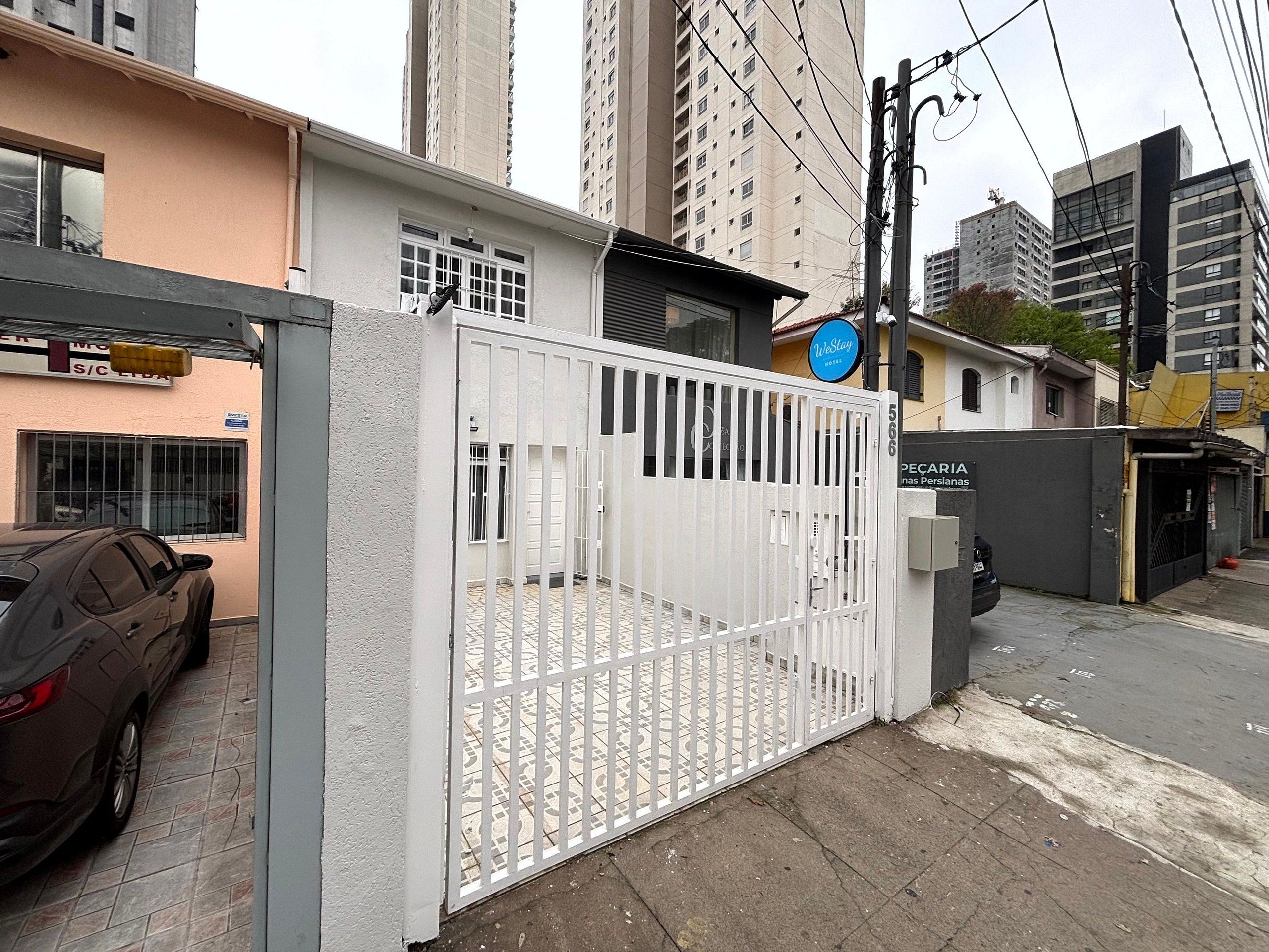 Una entrada con puerta metálica a un edificio con un cartel que dice 'WeStay Hotel' y un cartel que dice 'PECARIA nas Persianas'.