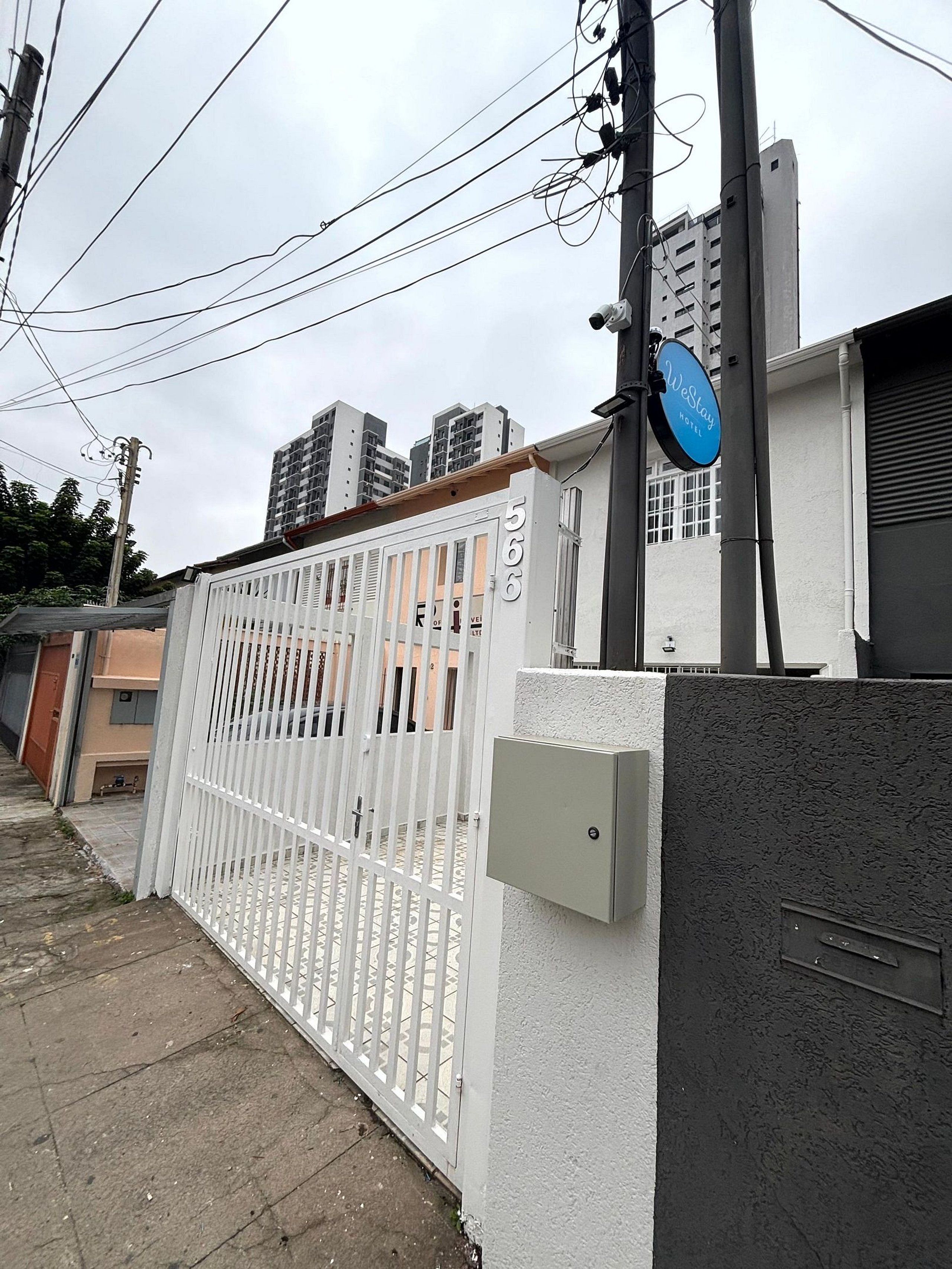 Propiedad privada con cerramiento, valla blanca, letrero azul que indica un hotel y una caja de servicios en la pared.
