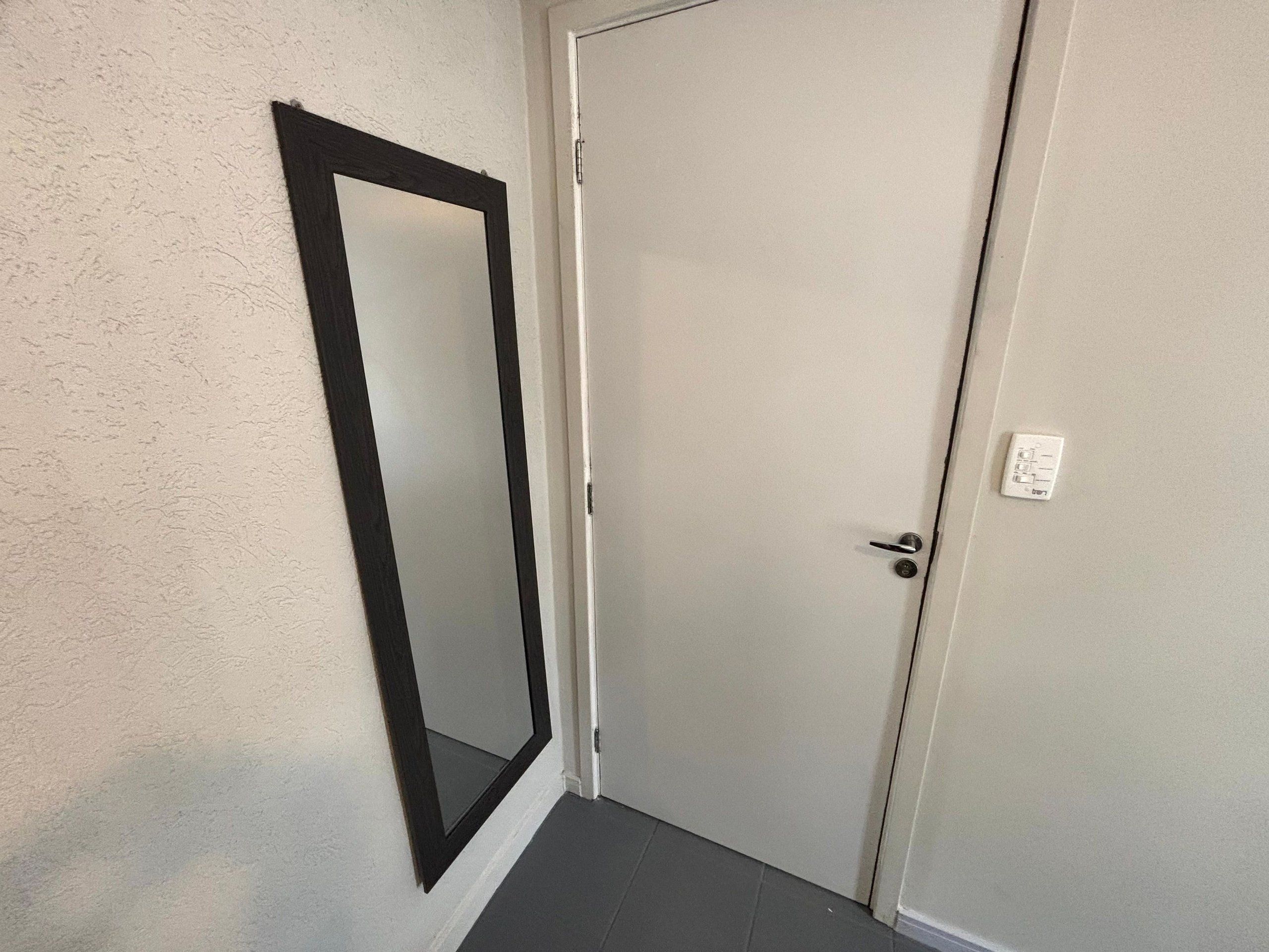 Une porte fermée, un mur blanc et un miroir à cadre noir sur le côté gauche.