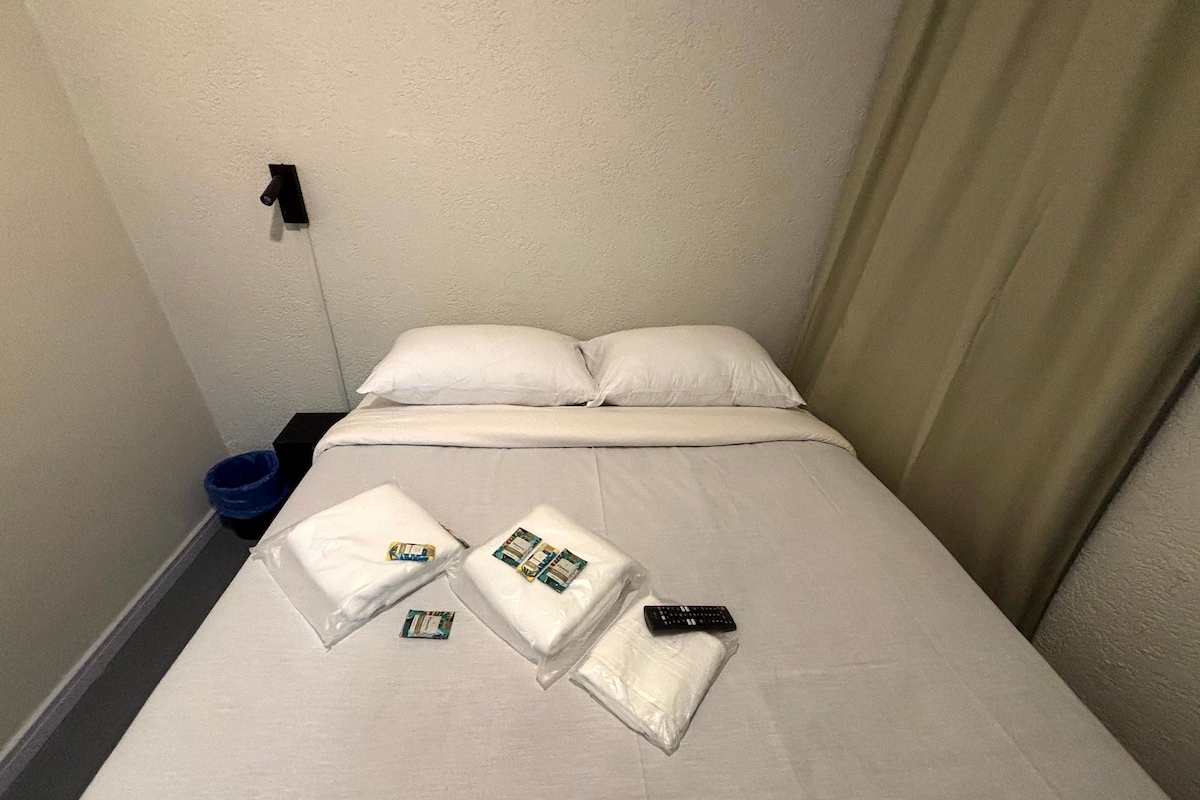 Quarto de hotel com cama, almofadas, controle remoto e artigos de higiene pessoal.