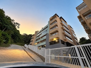 Un edificio residencial de varios pisos con balcones, un sendero empedrado y una valla blanca.