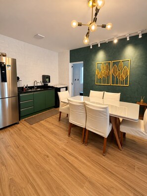 Una cocina moderna con refrigerador empotrado, un área de comedor con mesa y sillas, y una pared con arte decorado con motivos de hojas.