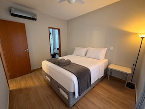 Un dormitorio con cama, mesita de noche, lámpara, armario y aire acondicionado.