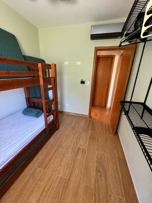 Une pièce de taille modeste comprenant un lit superposé, une petite kitchenette et une porte donnant sur une autre pièce.