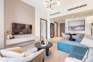 A modern living room with a flat-screen TV, a dining area with a table and chairs, and a sofa. - Resort-Style 1BR with Beach Access and a Balcony Overlooking Scenic Mountains (Khor Fakkan)