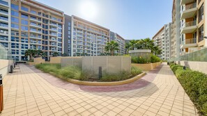 Un immeuble résidentiel moderne à plusieurs étages, doté d’un espace paysager central avec un élément circulaire et d’une allée dallée.