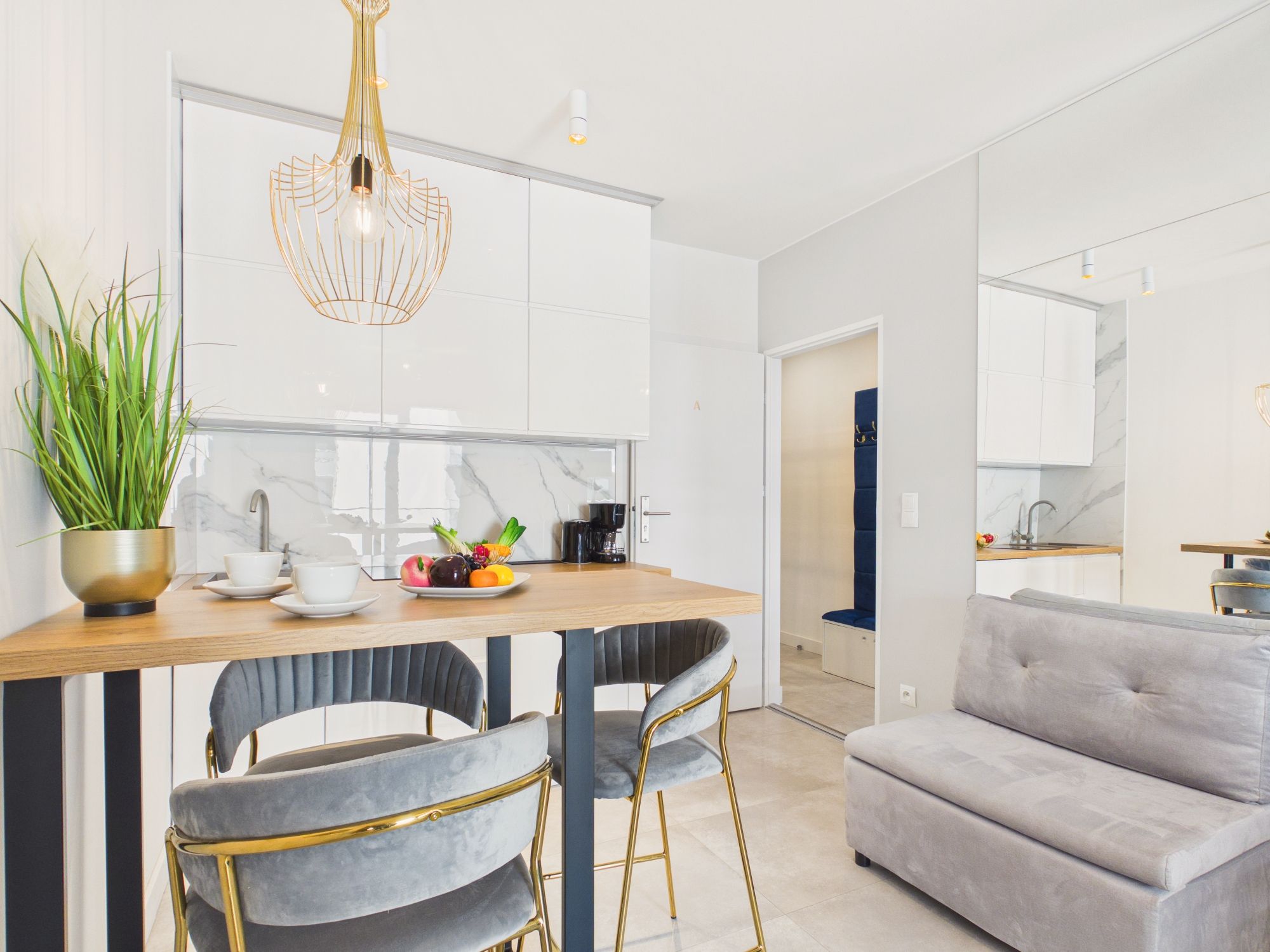 A modern kitchen with white cabinets, a wooden countertop, and a dining area with two grey upholstered chairs and a grey sofa.