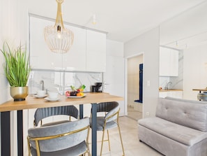 Cocina moderna con armarios blancos, encimera de madera y comedor con dos sillas tapizadas de gris y un sofá gris.