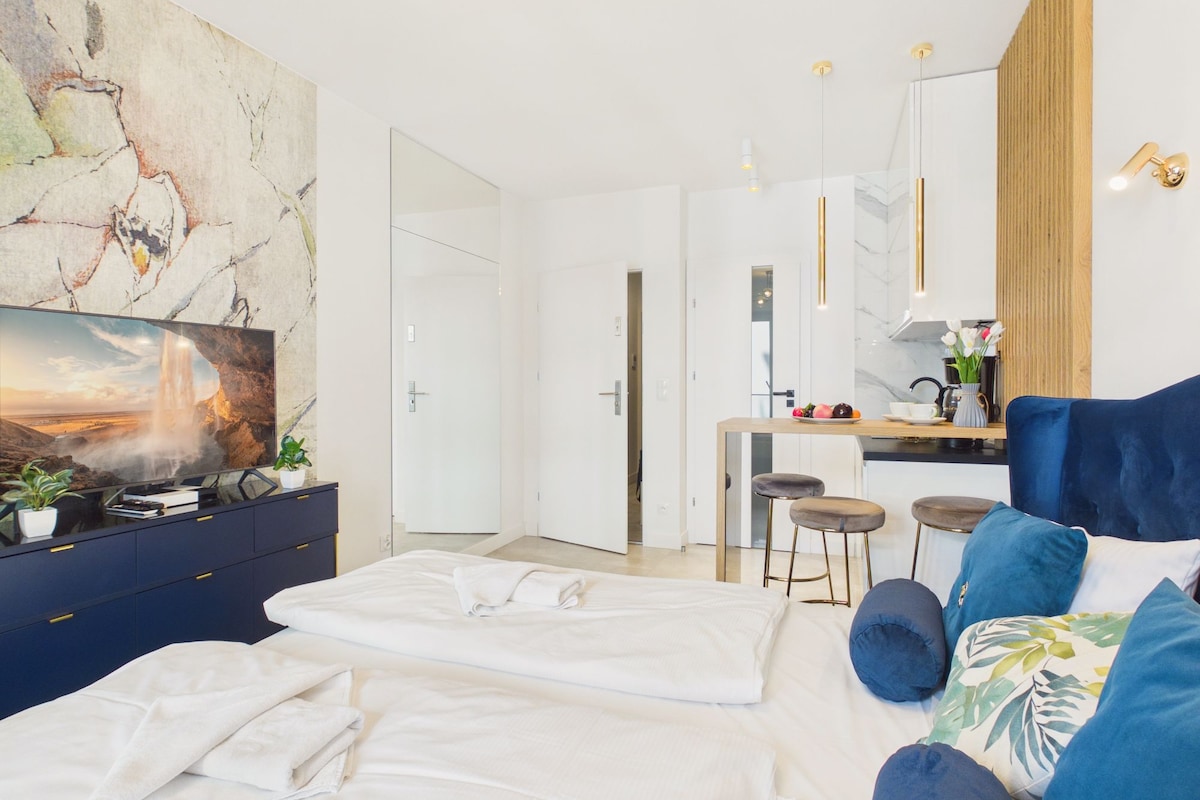 Ein modernes Hotelzimmer mit einem Bett, einem Schreibtisch, einem Sessel, einem Fernseher und einem großen abstrakten Gemälde an der Wand.