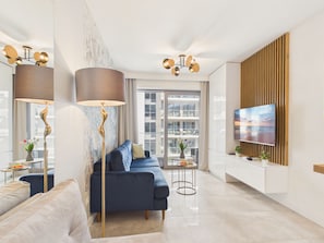 Ein modernes Wohnzimmer mit einem blauen Sofa, einer Stehlampe, einem Fernseher an einer Wand aus Holzpaneelen und einem großen Fenster.