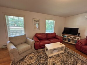 Ein Wohnzimmer mit einem beigen Sofa, einem roten Ledersofa, einem weißen Couchtisch und einem Fernseher auf einem Holzständer.