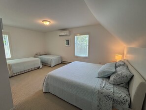 Ein Schlafzimmer mit zwei Einzelbetten, einem großen Bett, einem Nachttisch mit Lampe und einem Fenster mit Jalousien.