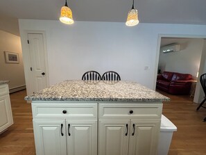 A kitchen with a granite countertop, white cabinetry, and two pendant lights. - Ebb Tide Way Wells Retreat (Wells)