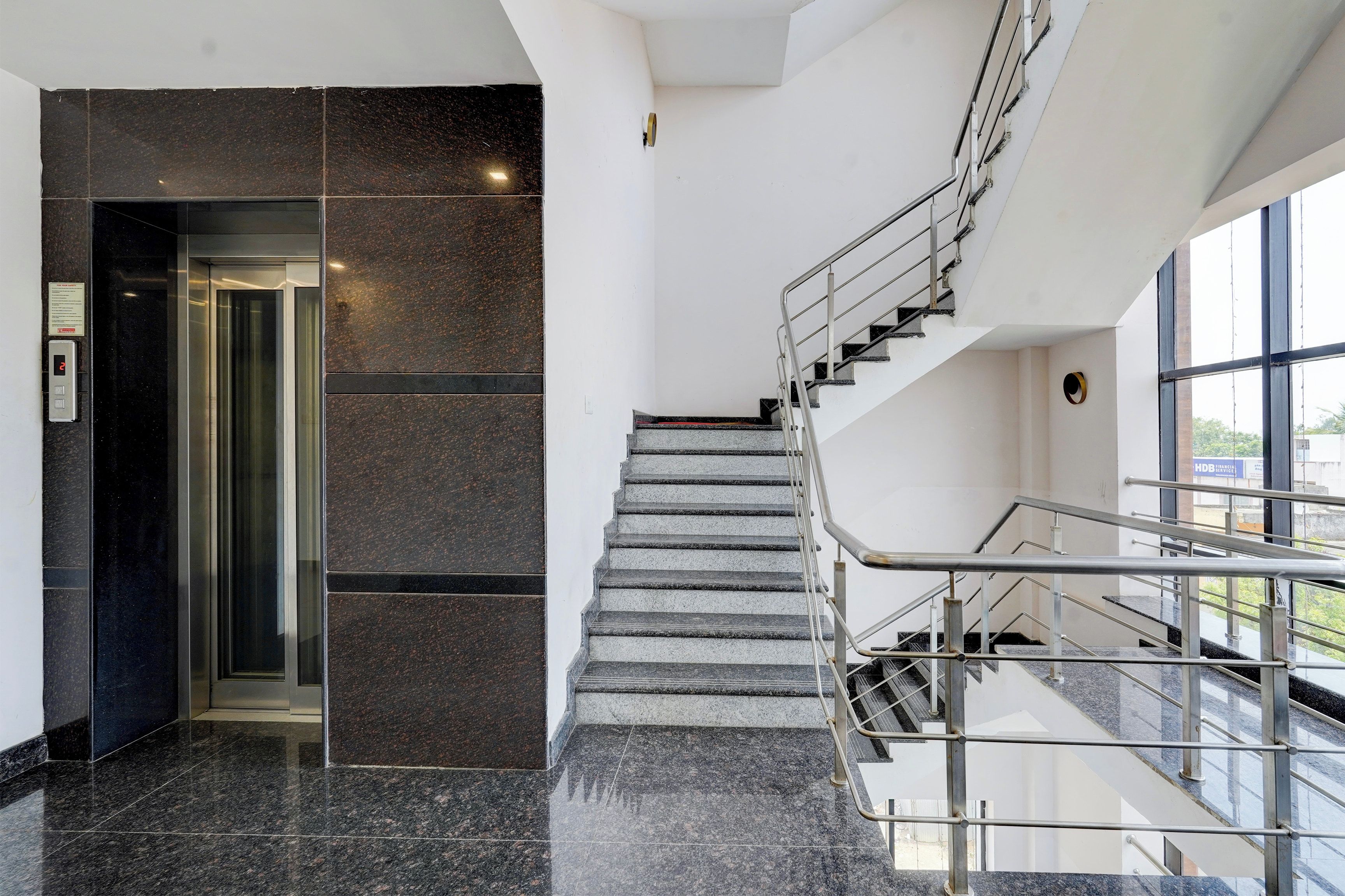 Un interior moderno con piso de mármol, una escalera con barandillas de metal y un ascensor de vidrio.