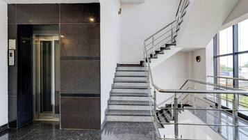 Un interior moderno con piso de mármol, una escalera con barandillas de metal y un ascensor de vidrio.