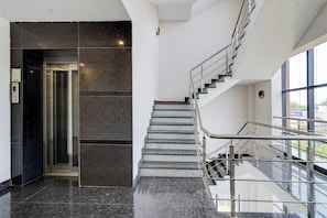 Un interior moderno con piso de mármol, una escalera con barandillas de metal y un ascensor de vidrio.