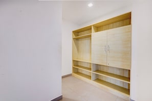 Una habitación con un armario de madera, varios estantes y suelo de baldosas.