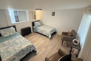 A hotel room with two beds, a small sofa, a nightstand, and a window with blinds. - Charming 4 bedroom 2 bath house in Hallandale (Hallandale)