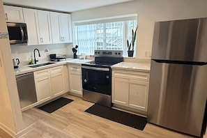 A modern kitchen with white cabinets, stainless steel appliances, and a window with blinds. - Charming 4 bedroom 2 bath house in Hallandale (Hallandale)