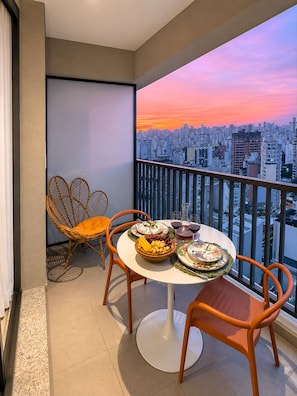A balcony with a cityscape view, a round table with plates and glasses, and wicker chairs. - SETIN 2304 (São Paulo)
