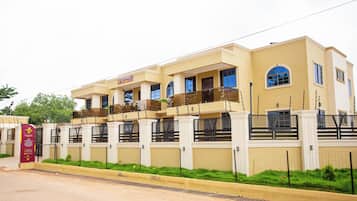A multi-story hotel with a gated entrance, a signboard, and a well-maintained lawn.
