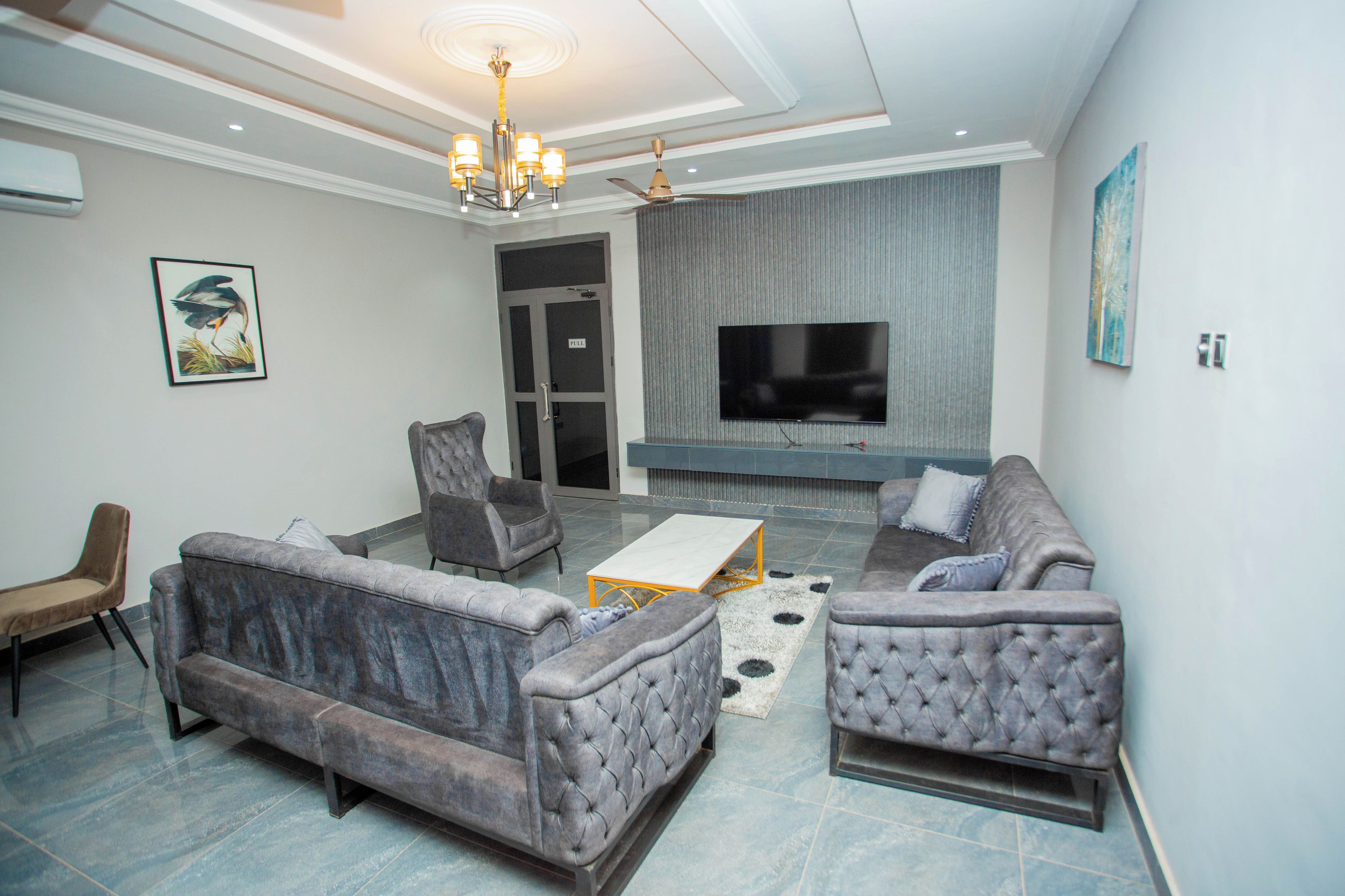 A modern living room with a grey sofa set, a coffee table, and a flat-screen TV mounted on the wall.