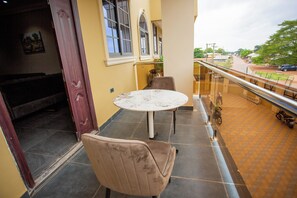 A balcony with a round table and two chairs, overlooking a street with parked cars and greenery. - Gateway Lodge Tamale  - Where Comfort Finds It's Finest Expression (Tamale)