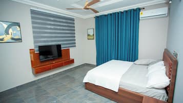 A bedroom with a bed, a television, a ceiling fan, and an air conditioning unit.