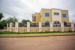 A multi-story building with a beige facade, a gated entrance, and a visible balcony on the second floor.
