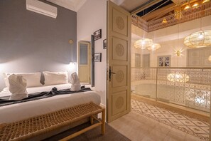Habitació d'hotel amb llit, una banca, un armari i un balcó amb barana decorativa i llums.