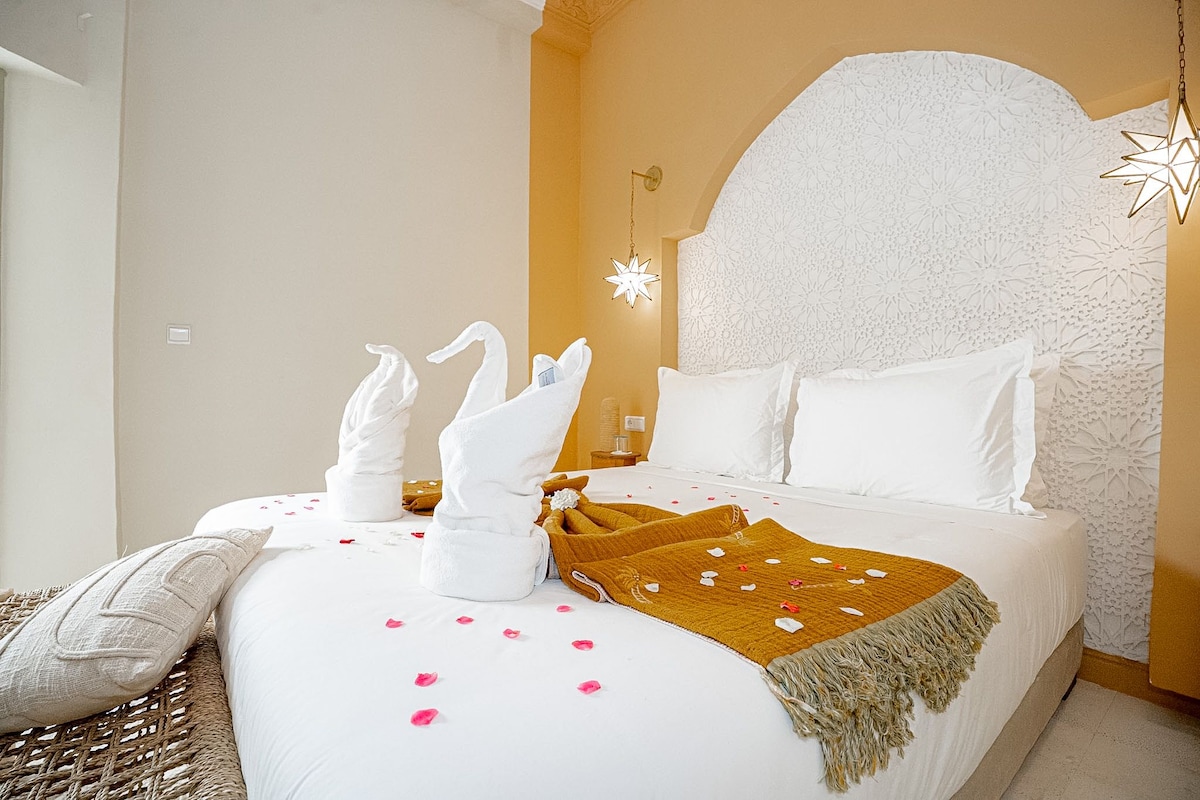 Una habitació d'hotel amb un llit gran, roba de llit blanca, un panell decoratiu al capçal i una làmpada amb forma d'estrella.
