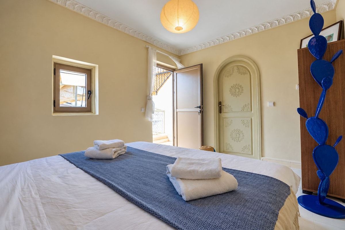 Habitació d'hotel amb un llit, una finestra, una porta i una escultura blava decorativa.