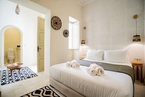 Una habitació d'hotel amb un llit, una taula de nit, un penjador, un rellotge fixat a la paret i una porta que dona al bany.